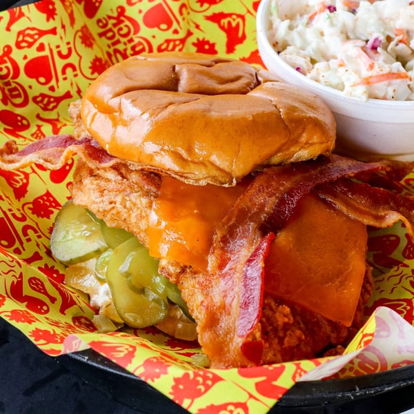 A fried chicken sandwich with bacon, pickles, and cheese, served with coleslaw.
