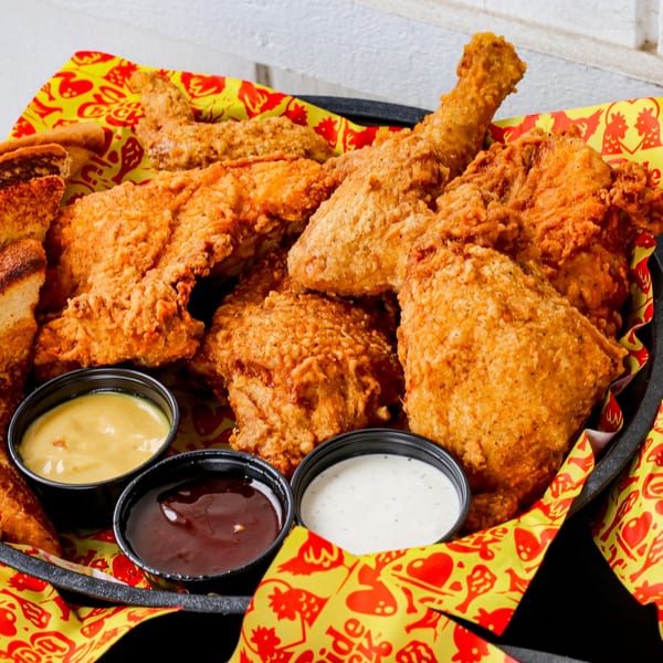 Crispy fried chicken pieces, toast, and three dipping sauces in a black basket with yellow paper.