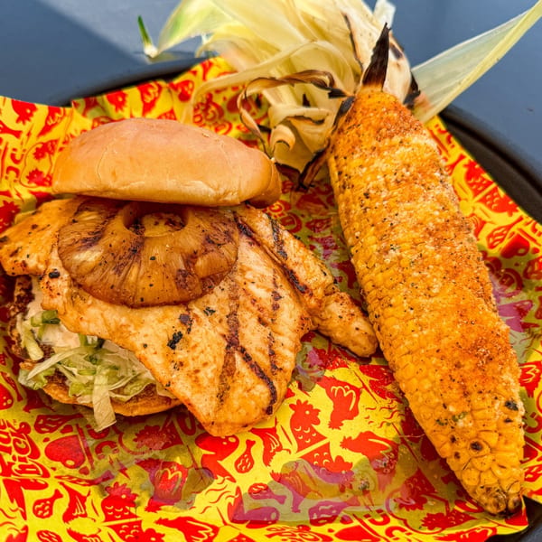 Grilled chicken sandwich with pineapple and lettuce, served with seasoned corn on the cob.