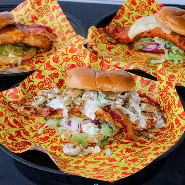 Three Side Chick chicken sandwiches in baskets, each with unique toppings, on branded yellow and red paper.