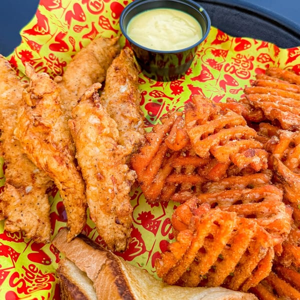 Crispy chicken tenders, waffle fries, Texas toast, and dipping sauce on patterned paper.