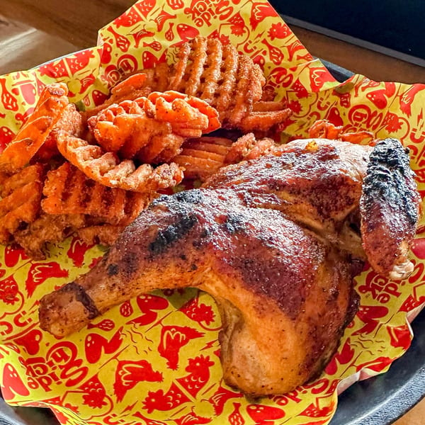 A grilled chicken leg and thigh with waffle fries on red and yellow patterned paper.