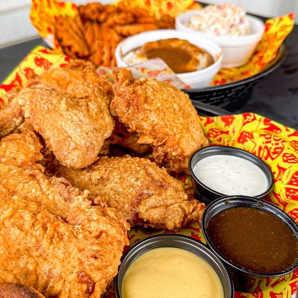 Crispy fried chicken pieces with various dipping sauces, waffle fries, and coleslaw in a basket.